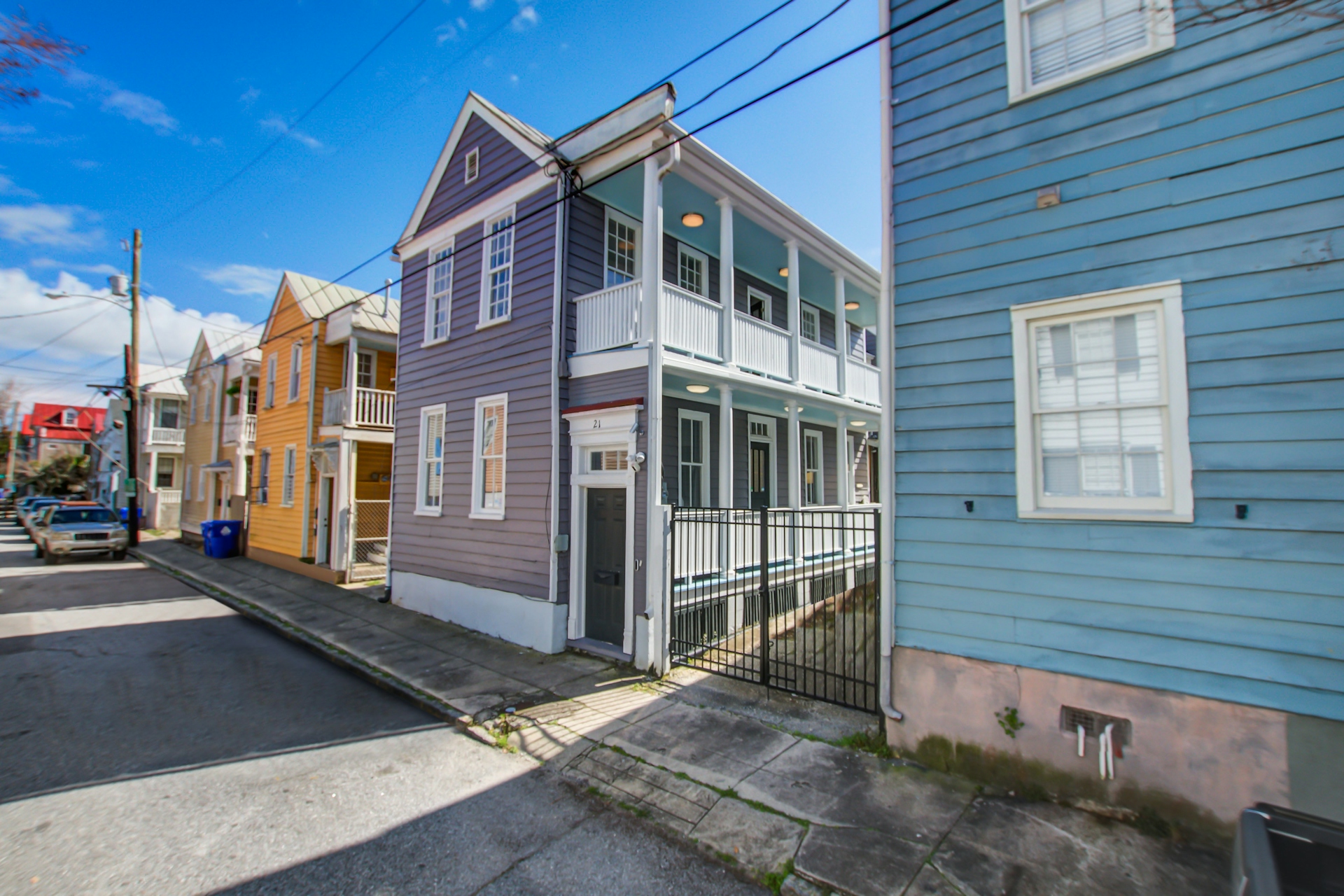 Three-story Charleston single with lavender siding, white trim, double front porches, black front door, and metal gate — street view.