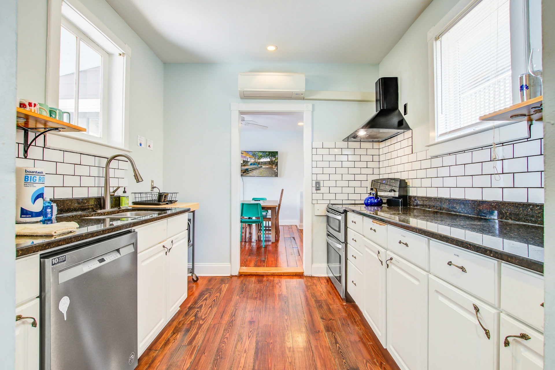 Galley kitchen from the rear showing both cabinetry runs, dishwasher, range with hood, mini-split AC, and doorway to dining room.