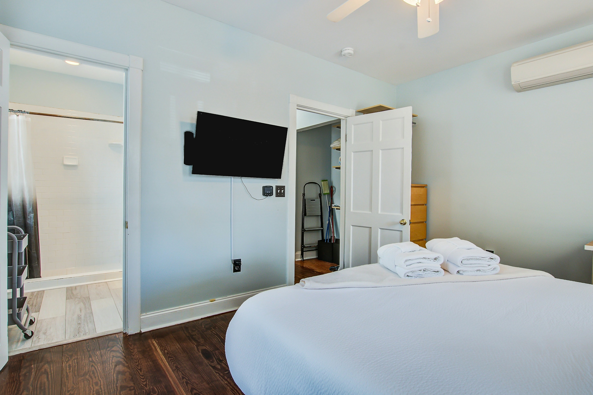 Bedroom with queen bed, wall-mounted TV, mini-split AC, and open doorways to ensuite walk-in shower and closet storage.