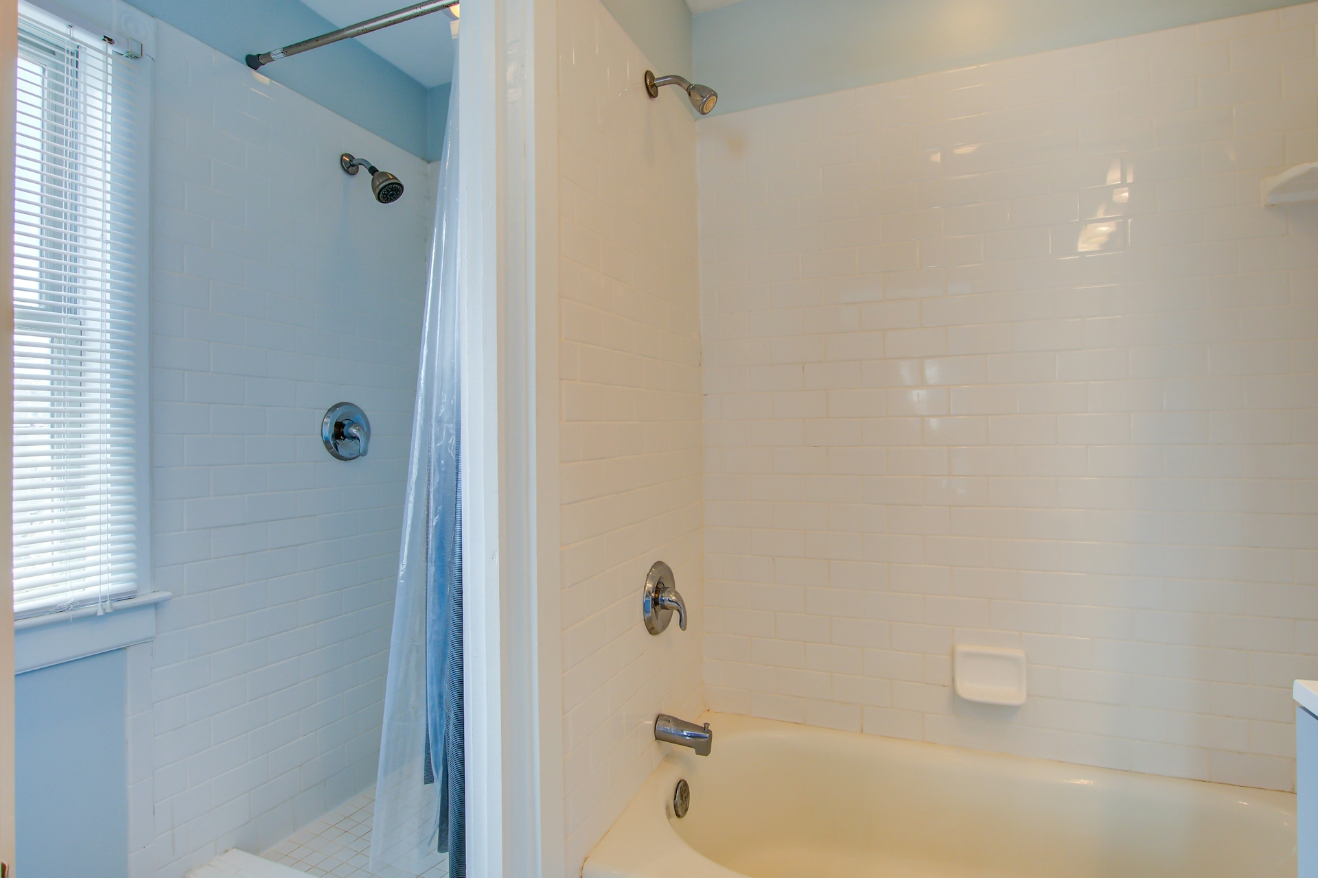 Bathroom with stand-up tiled shower stall and adjacent tub-shower combo, both with subway tile and shower curtains.