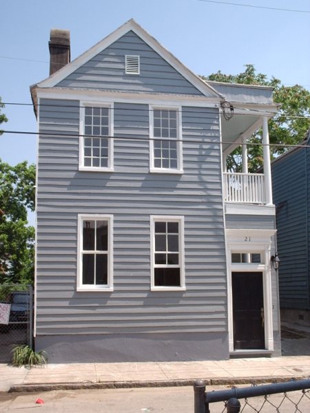 The restored front facade with Charleston single-style trim, side balcony, dormer-style attic vent, and the address reset above the door.