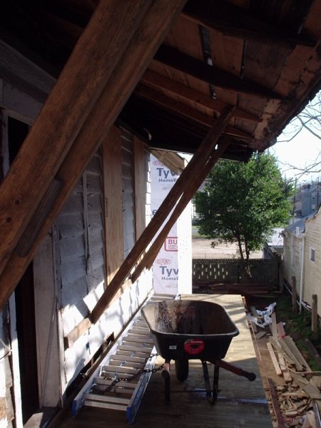 Mid-construction view: roof framing exposed, Tyvek wrap, and porch-deck work underway.