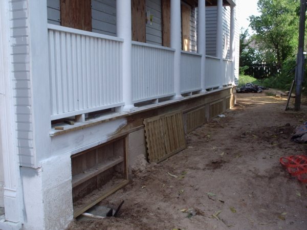Porch skirt going in, with column bases set and lattice frames being built.